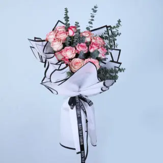 A hand holding a bouquet of blush pink roses wrapped in white paper