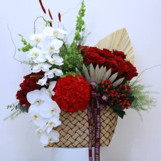 A large basket overflowing with red roses, white orchids, red carnations, and other vibrant blooms.