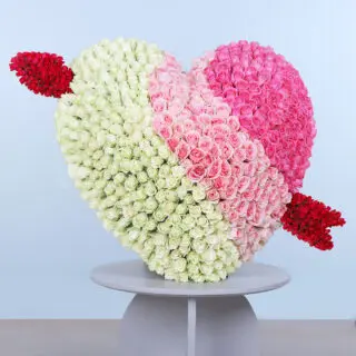 A heart-shaped arrangement of light pink, dark pink and white roses with a bow and arrow.
