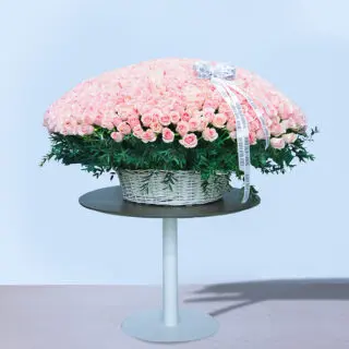 A large basket overflowing with hundreds of pink roses on a white table.