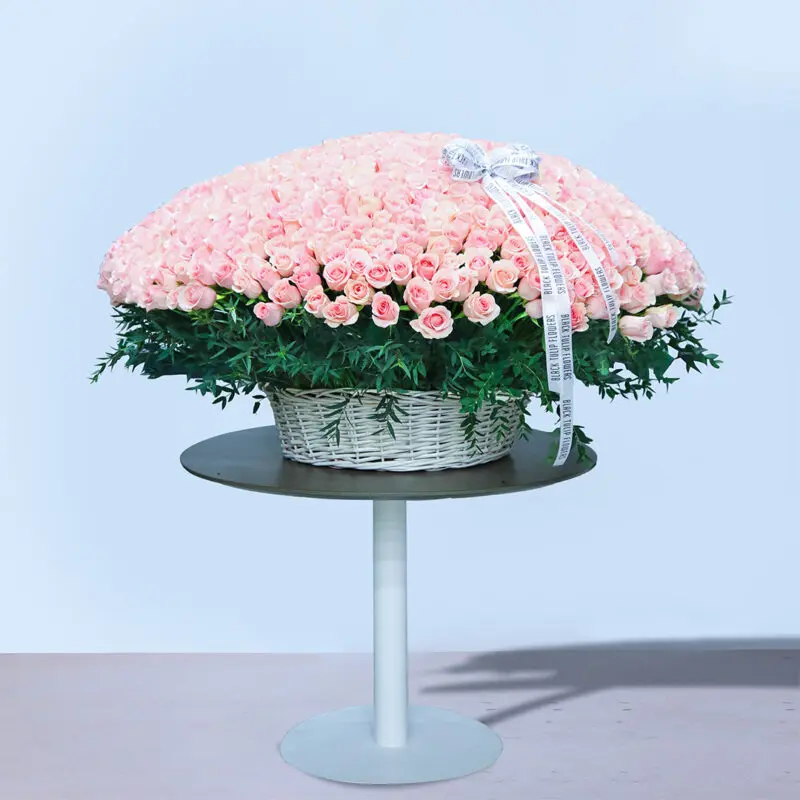A large basket overflowing with hundreds of pink roses on a white table.