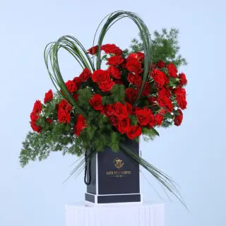 Elegant arrangement of red roses in a black box accented with steel grass in heart shape.