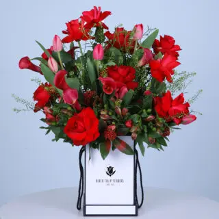 A charming mix of red and pink roses and tulips, creating a cheerful atmosphere in a crisp white box.