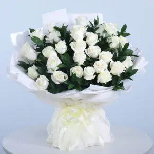 A bouquet of pristine white roses wrapped in white paper with a soft yellow ribbon.
