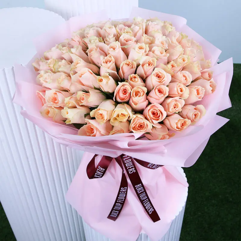 Peach Grace Bouquet An elegant bouquet featuring fresh peach roses wrapped in blush pink paper and tied with a maroon ribbon.