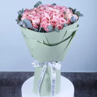 Elegant pastel pink roses arranged with eucalyptus, wrapped in stylish sage green paper.