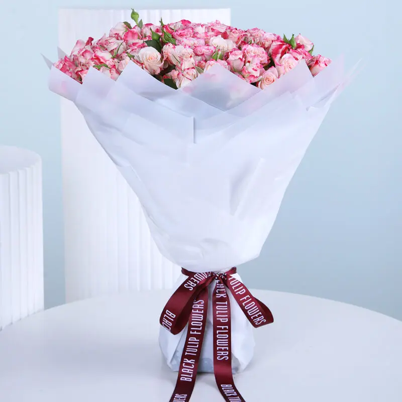 A bouquet of fresh 50 pink baby roses wrapped elegantly in a white paper and tied with a black knot.