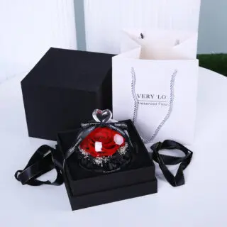 A preserved red rose in a glass dome inside a black gift box, with a white gift bag and black ribbon
