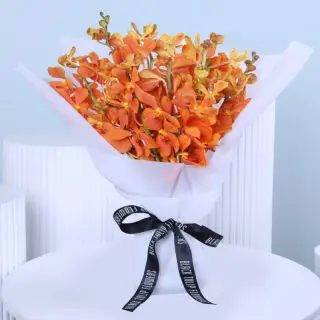 A hand-tied bouquet of vibrant orange mokara orchids wrapped in white paper and finished with a black ribbon.