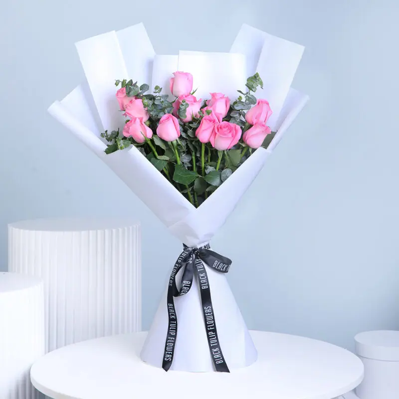 12-pink-roses-bouquet A wrapped bouquet containing 12 pastel pink roses and green eucalyptus, tied with a black ribbon.