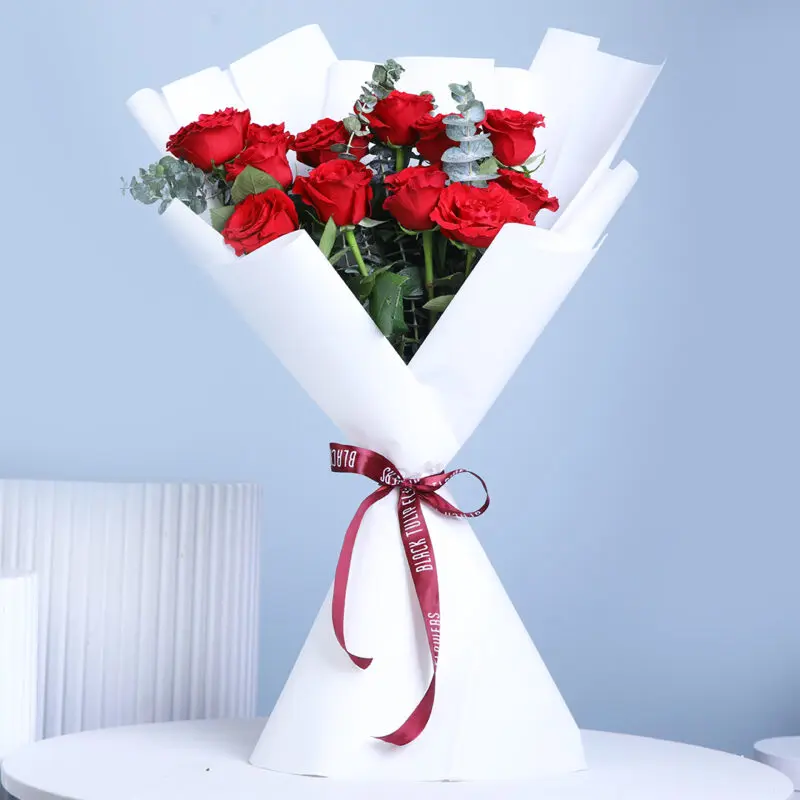 12-red-roses-bouquet A bouquet containing 12 vibrant red roses with green eucalyptus, wrapped in white and secured with a dark red ribbon.