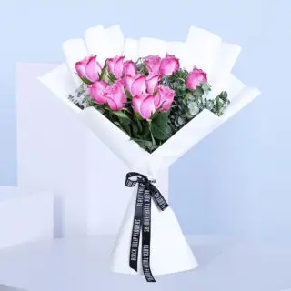 A beautifully arranged bouquet of a dozen vibrant purple roses with green leaves, wrapped in white.