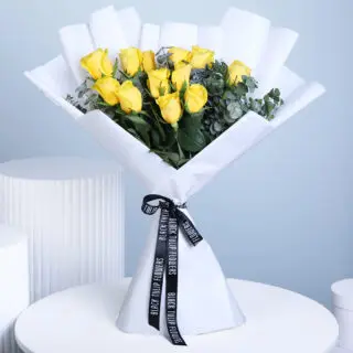 A bouquet of a dozen bright yellow roses with green eucalyotus, wrapped in white and tied with a black ribbon.
