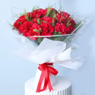 A beautiful bouquet of vibrant red roses and delicate white lepidium, wrapped in white and tied with a red ribbon.