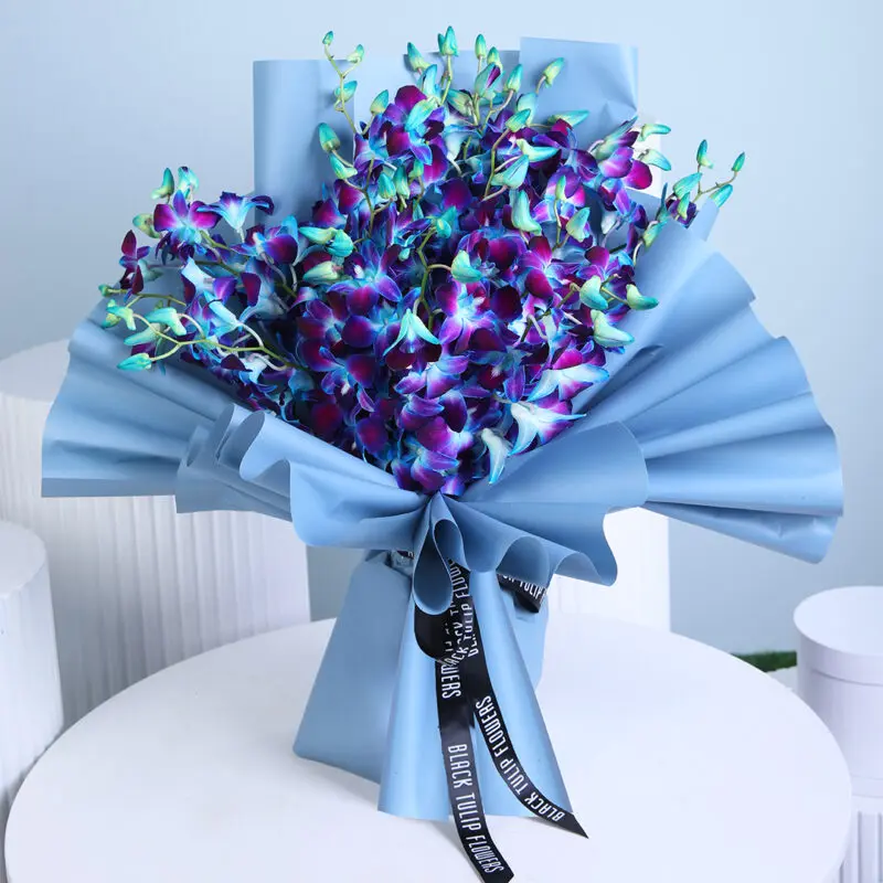A beautifully wrapped bouquet of deep blue and purple orchids with hints of green, tied with a black ribbon.