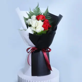 A bouquet of vibrant red roses and pure white roses, wrapped in contrasting black and white paper and tied with a red ribbon.