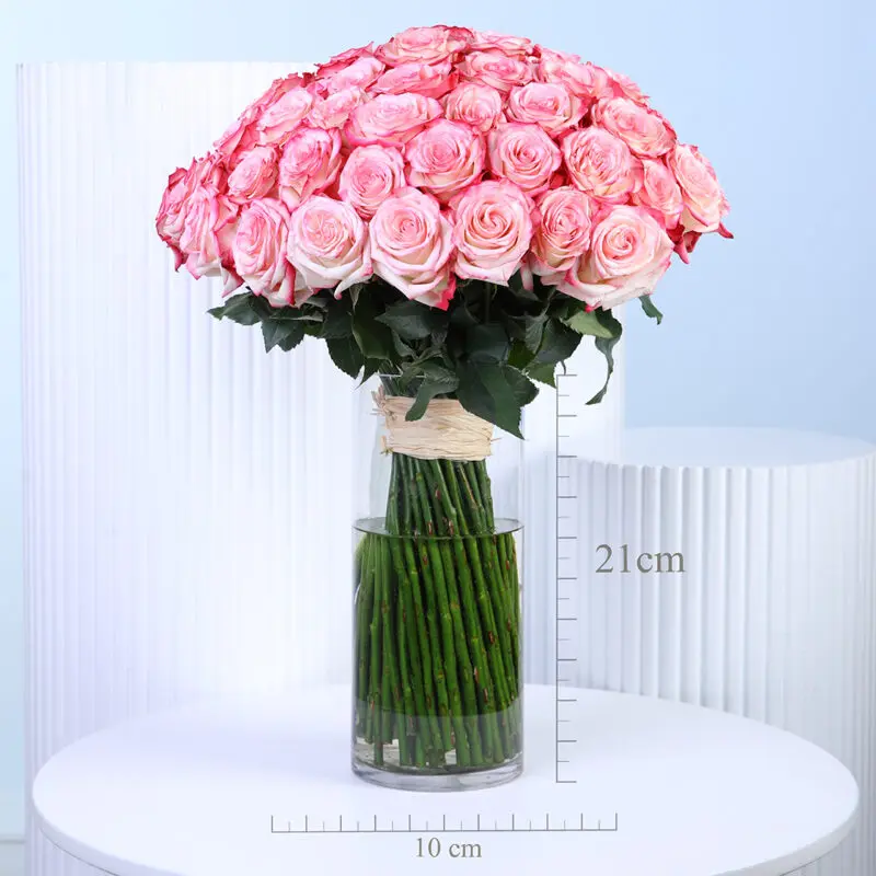 bi-colour-pink-rose-vase A large bouquet of 100 vibrant two-tone pink roses, with petals from a lighter pink at the center to a deeper, more saturated pink at the edges, is presented in a tall, clear glass cylindrical vase.