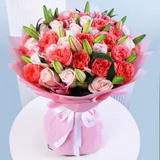 A vibrant bouquet of pink roses and white lilies wrapped in pink paper with a white ribbon presented on a white round table.