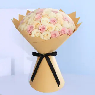 Bouquet of cream and pink roses wrapped in brown with a black ribbon.