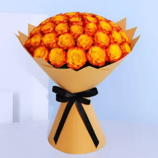 A large bouquet composed of numerous roses with bright yellow centers and vivid orange edges, wrapped in light brown paper and tied with a black ribbon.
