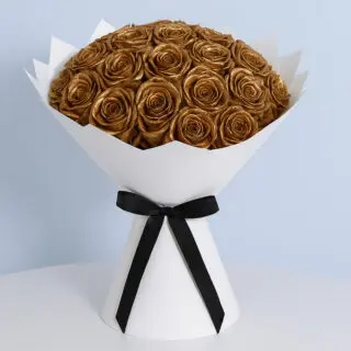 A bouquet of real roses painted in a brilliant metallic gold color, elegantly arranged and wrapped in crisp white paper with a black ribbon.
