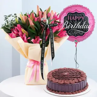 A birthday combo featuring a bouquet of pink lily flowers wrapped in light yellow wrap with a pink ribbon, a round pink "Happy Birthday" balloon and a round chocolate cake with chocolate frosting.