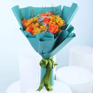 A bouquet of orange chrysanthemums and orange roses with white gypsophila and green thlaspi, wrapped in teal paper and tied with a green ribbon.