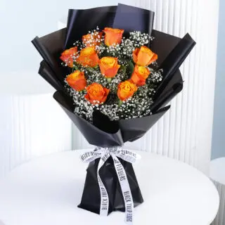 A bouquet of orange roses and white gypsophila, wrapped in black and elegantly tied with a white ribbon.