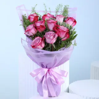 A bouquet of purple roses with green foliage, wrapped in translucent lavender paper and tied with a matching ribbon.