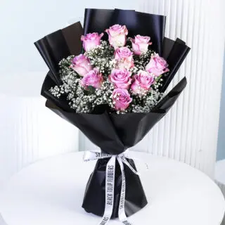 A luxurious bouquet featuring 10 purple roses and 5 stems of white gypsophila, stylishly wrapped in sleek black paper and tied with a white ribbon.