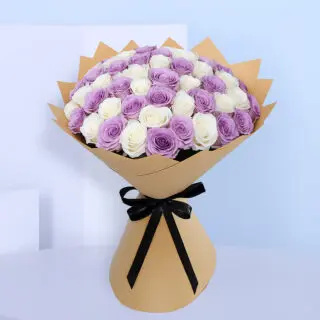 A large bouquet showing alternating layers of pure white roses and light purple roses, creating a serene bi-color effect. The bouquet is wrapped in a light brown paper and tied with a black ribbon.