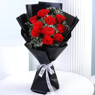 A bouquet of 10 vibrant red roses with white gypsophila (baby's breath) wrapped in black paper and tied with a black and white ribbon.