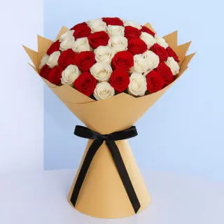 Freshly cut red and white roses arranged in a hand-tied bouquet, wrapped with brown and a contrasting black ribbon.