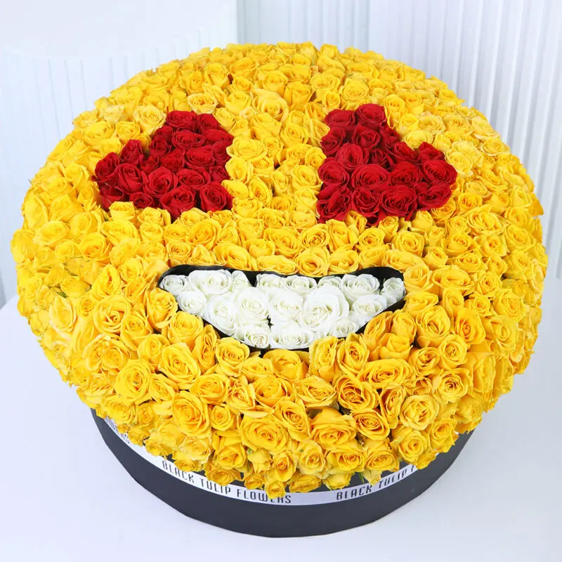 emoji-yellow-rose-box Emoji-inspired floral arrangement with yellow roses forming a round yellow face, red rose heart-shaped eyes, and a white rose smile, presented in a black round box.