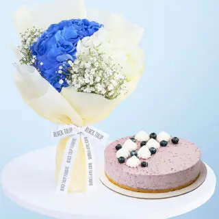 A flower combo featuring a bouquet of blue and white hydrangeas and baby's breath wrapped in cream and a purple-colored cheesecake.