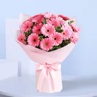 A large bouquet of 20 pink Gerbera daisies with green leaves, wrapped in light pink paper and tied with a matching pink satin ribbon.