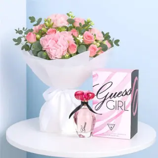 A Guess Girl EDT for Women with a White-wrapped bouquet of blush hydrangea, pink spray roses, and greenery on a table.