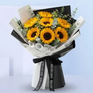 A hand-tied bouquet of bright yellow sunflowers and green eucalyptus stems wrapped in a stylish black and white ribbon and tied with a black ribbon.