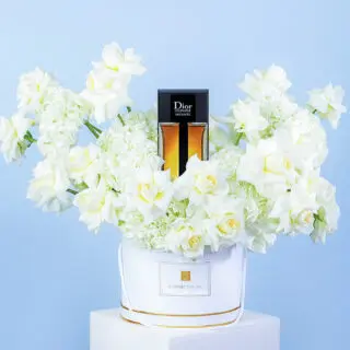 White box arrangement of white roses and hydrangeas featuring a Dior Homme Intense perfume bottle in the center.