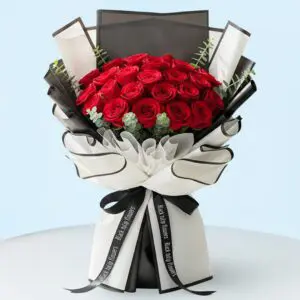 A hand-tied bouquet of vibrant red roses arranged with green eucalyptus stems and wrapped in stylish black and white secured with a black ribbon.