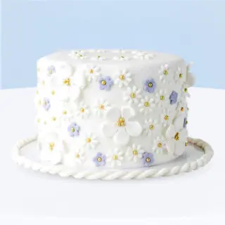 White flower-themed fondant cake decorated with pastel lilac flowers and gold pearls.