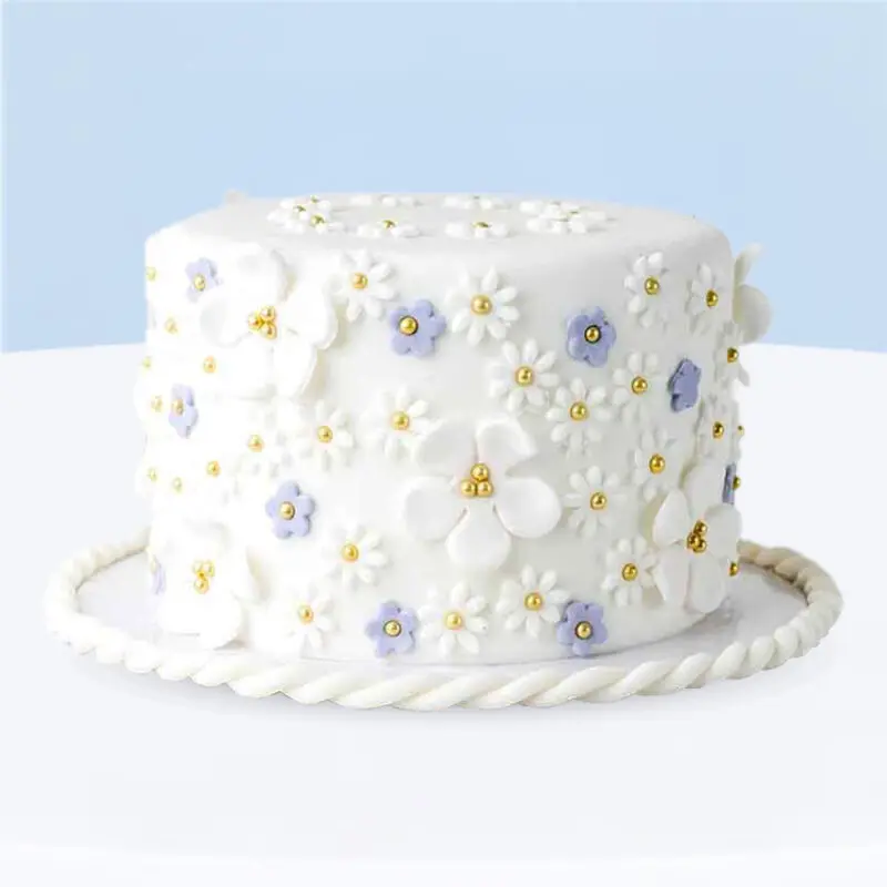 White flower-themed fondant cake decorated with pastel lilac flowers and gold pearls.