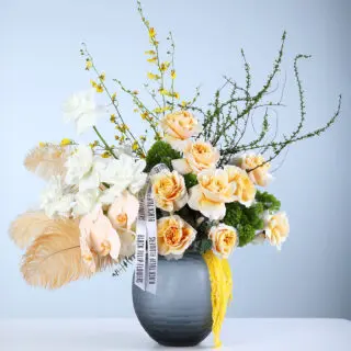 Floral arrangement featuring roses, orchids, feathers, oncidium, and trichelium in an elegant grey vase, styled for luxury decor and gifting.