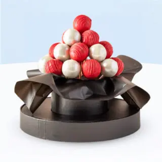 Festive gift box with 25 red and white chocolate-covered cake pops arranged in a clear round box with black ribbon.