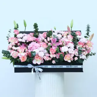 A rectangular gift box featuring lilies, ranunculus, hydrangeas, chrysanthemums, baby roses, lisianthus, and eucalyptus.