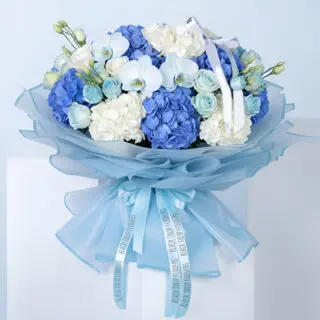 Bouquet featuring blue hydrangea, white hydrangea, roses, lisianthus, and orchid blooms in blue premium wrapping with a satin bow.