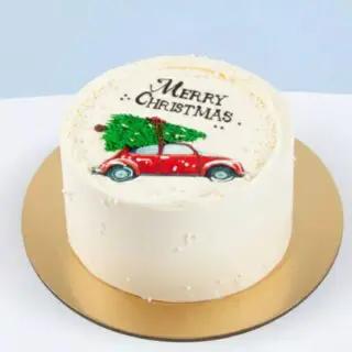 Festive Christmas car honey cake with white cream icing, Merry Christmas message and a red car carrying a Christmas tree on top, 720g.