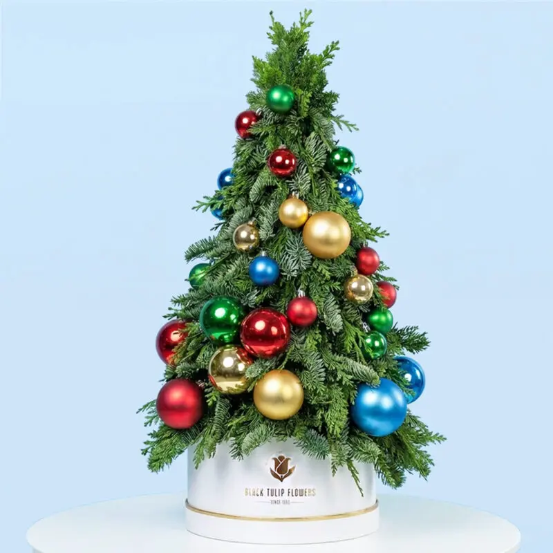 festive-tabletop-christmas-tree Tabletop Christmas tree with fresh green branches and colorful baubles in a white box.