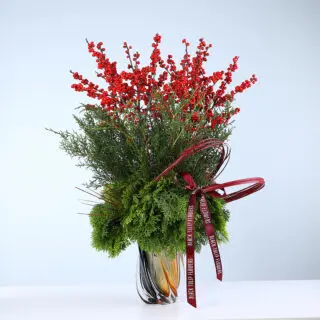 Christmas arrangement with red Ilex berries, Jennifer leaves, and festive greens in a designer vase.