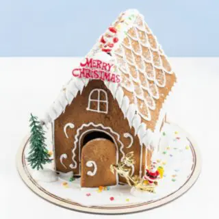 Mini Merry Christmas gingerbread house with white icing, Santa and reindeer decor, small tree and confetti on a round base, 650g.